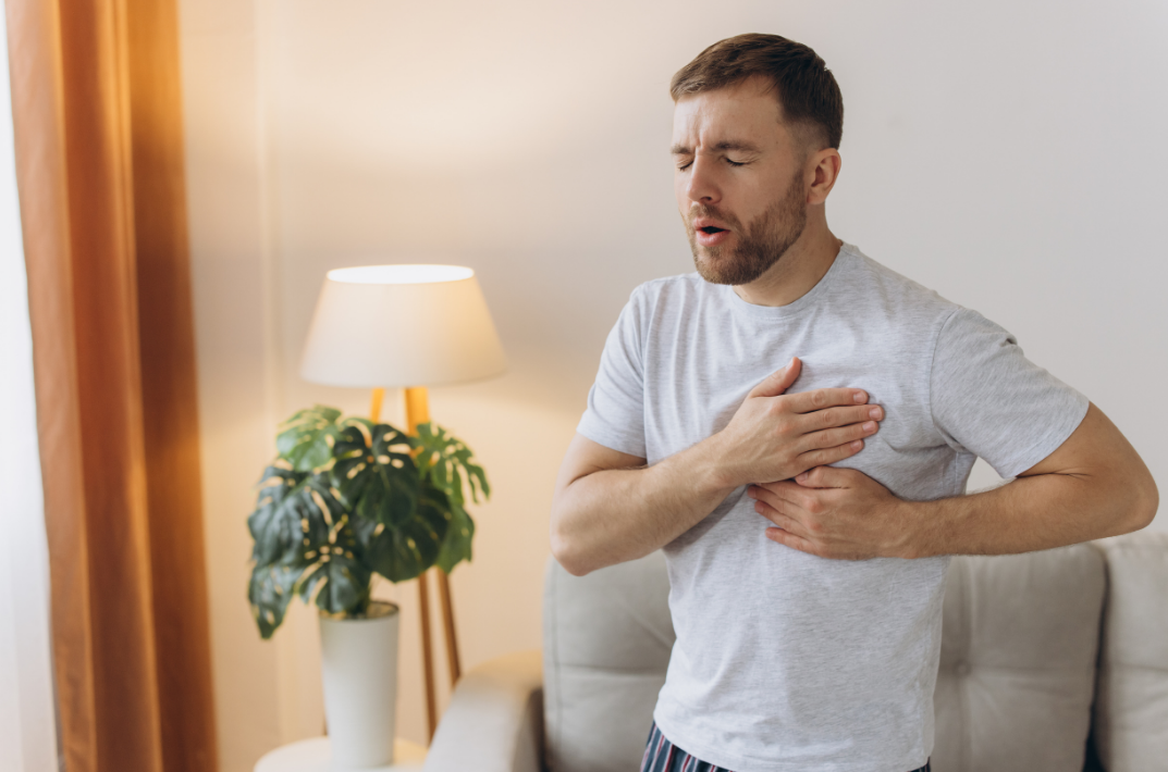 Man holding his chest and appearing to experience chest pain while standing in a living room.