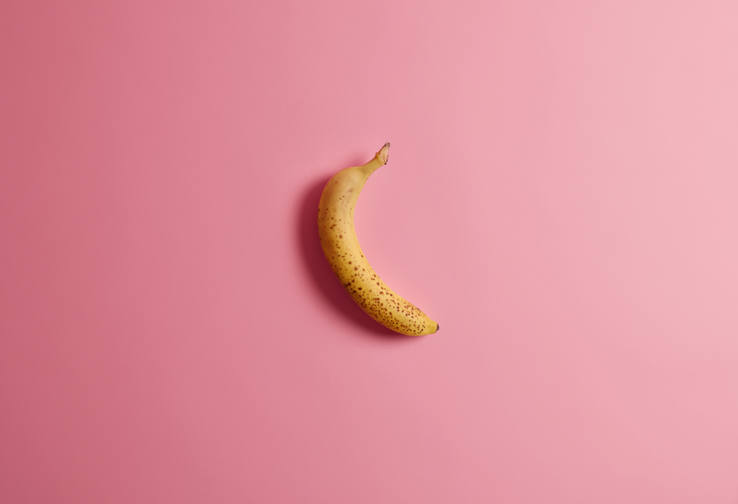 Ripe yellow banana placed on a pink background, symbolising penile curvature or Peyronie’s disease in a conceptual medical illustration.