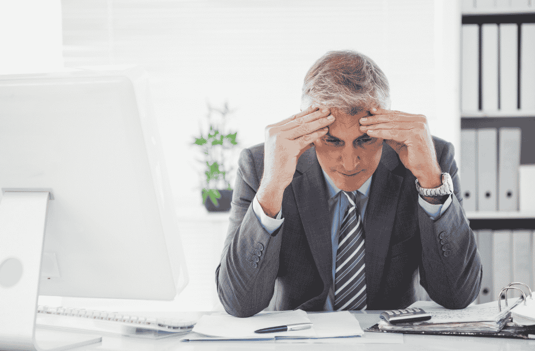 Businessman sitting at a desk with his head in his hands, showing the impact of work stress and lifestyle pressures on mental wellbeing.