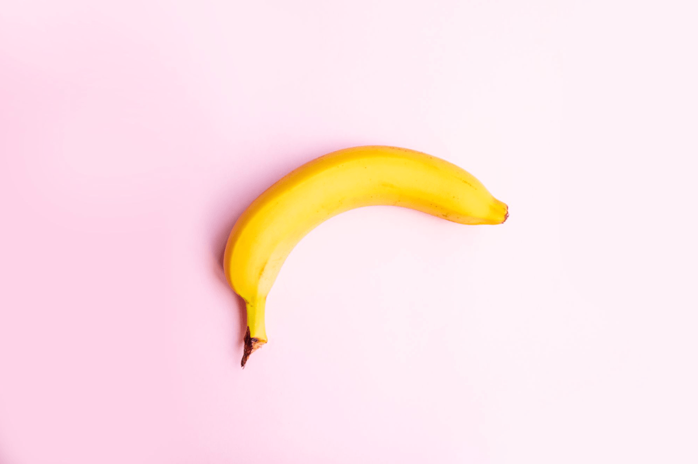 Banana on a pink background used as a visual representation of penile curvature associated with Peyronie's disease.
